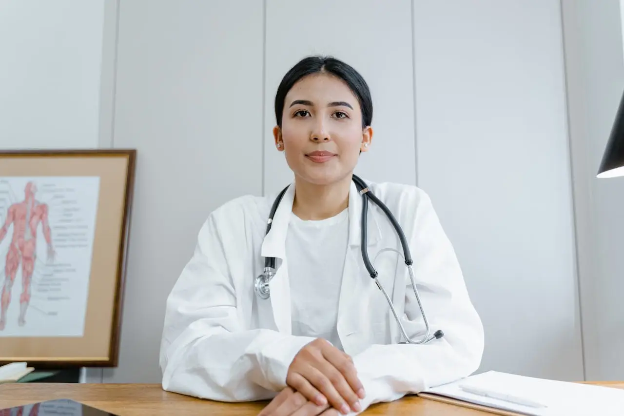 A female doctor confidently sits at her desk, ready for consultation in a medical office.